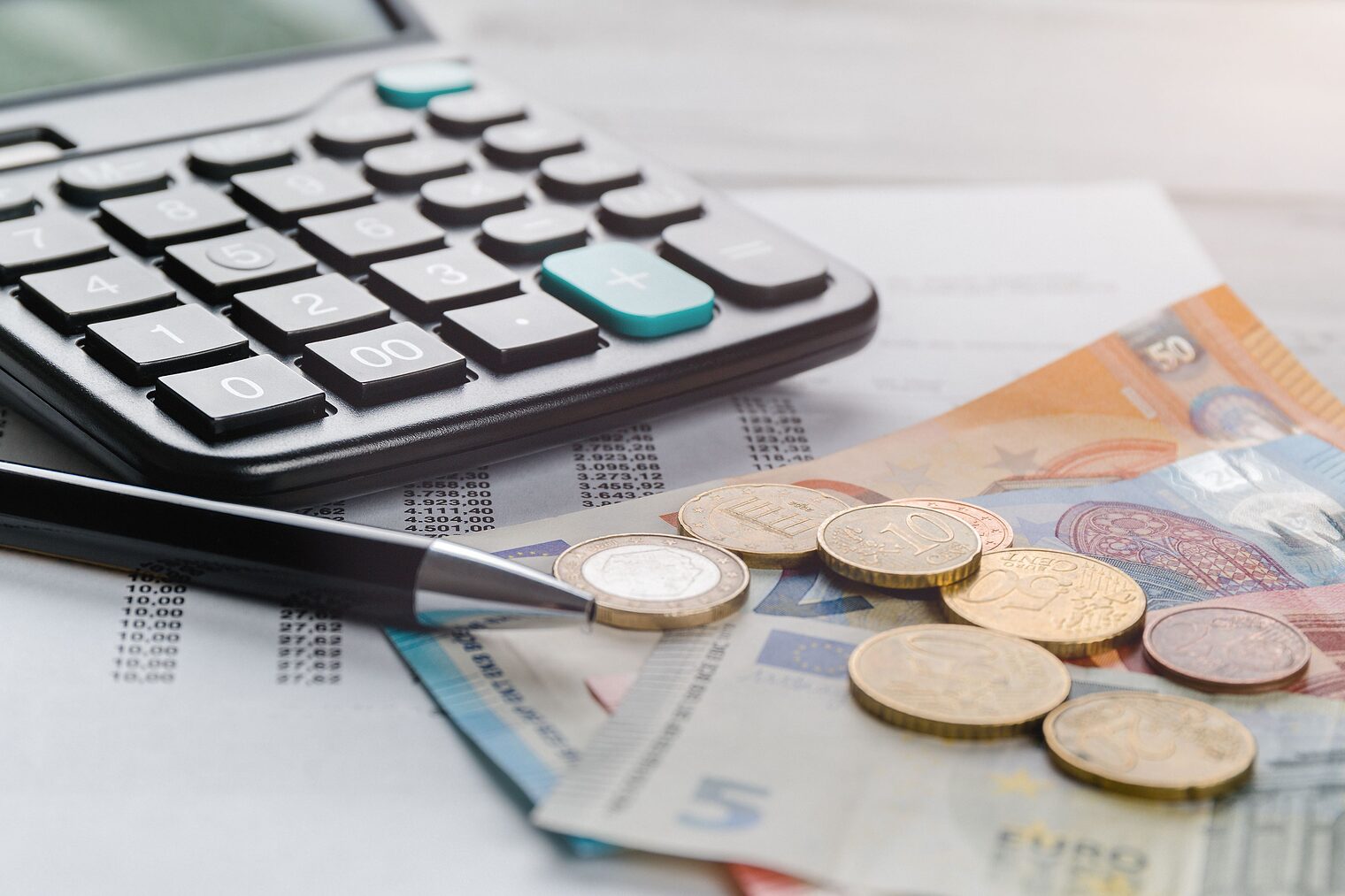 Taschenrechner, Geldscheine und Münzen, Stift und ausgedruckte Tabellenkalkulation