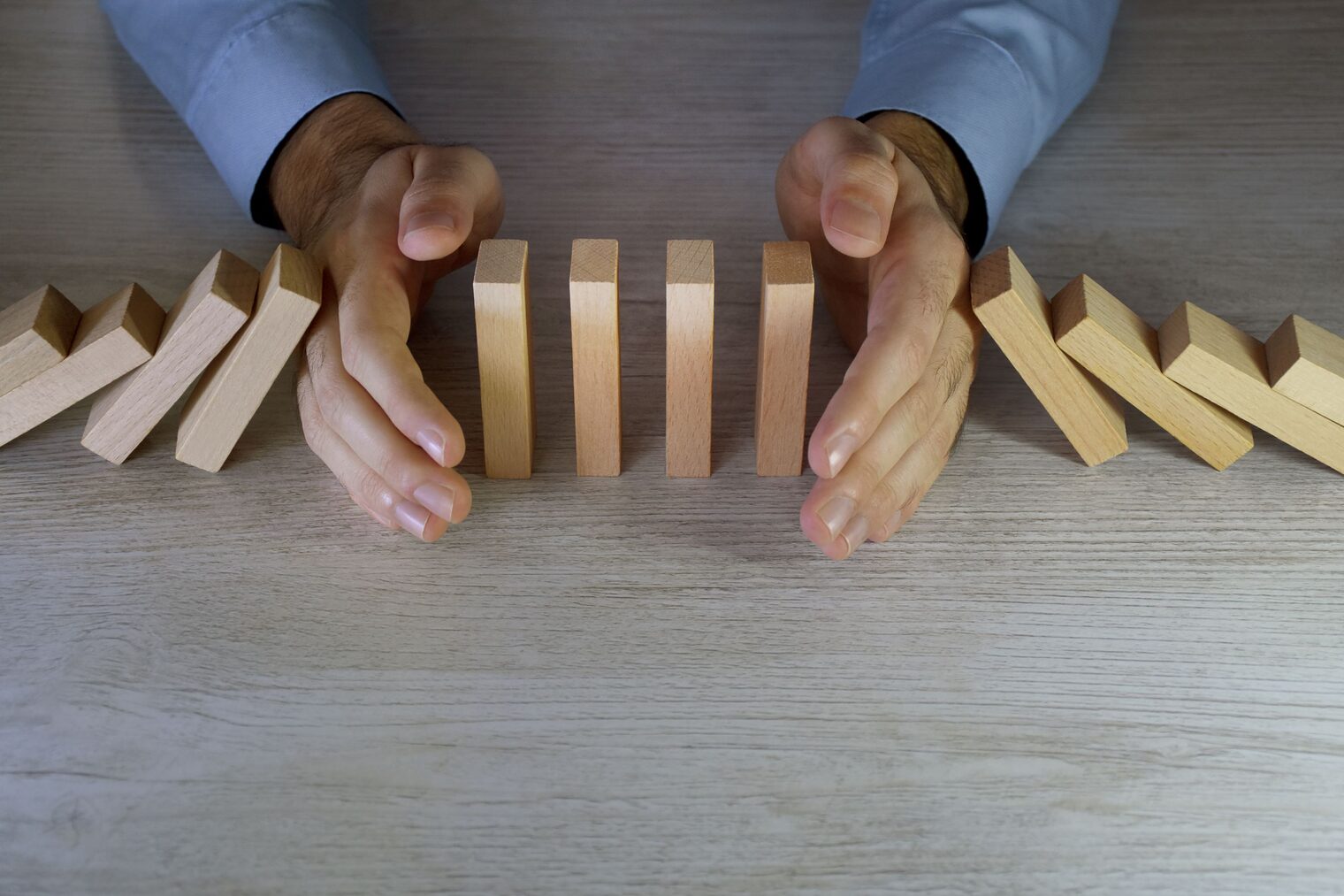 Eine Person versucht das Fallen von Domino-Steinen mit ihren Händen zu stoppen.