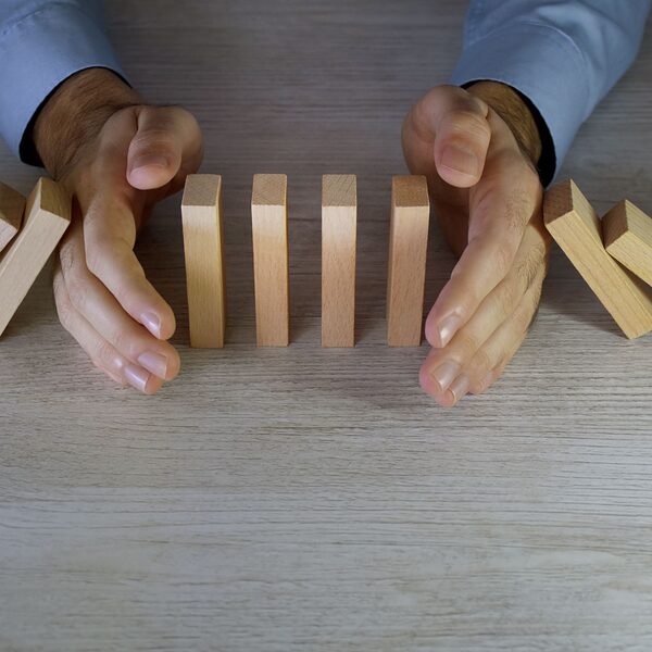 Eine Person versucht das Fallen von Domino-Steinen mit ihren Händen zu stoppen.