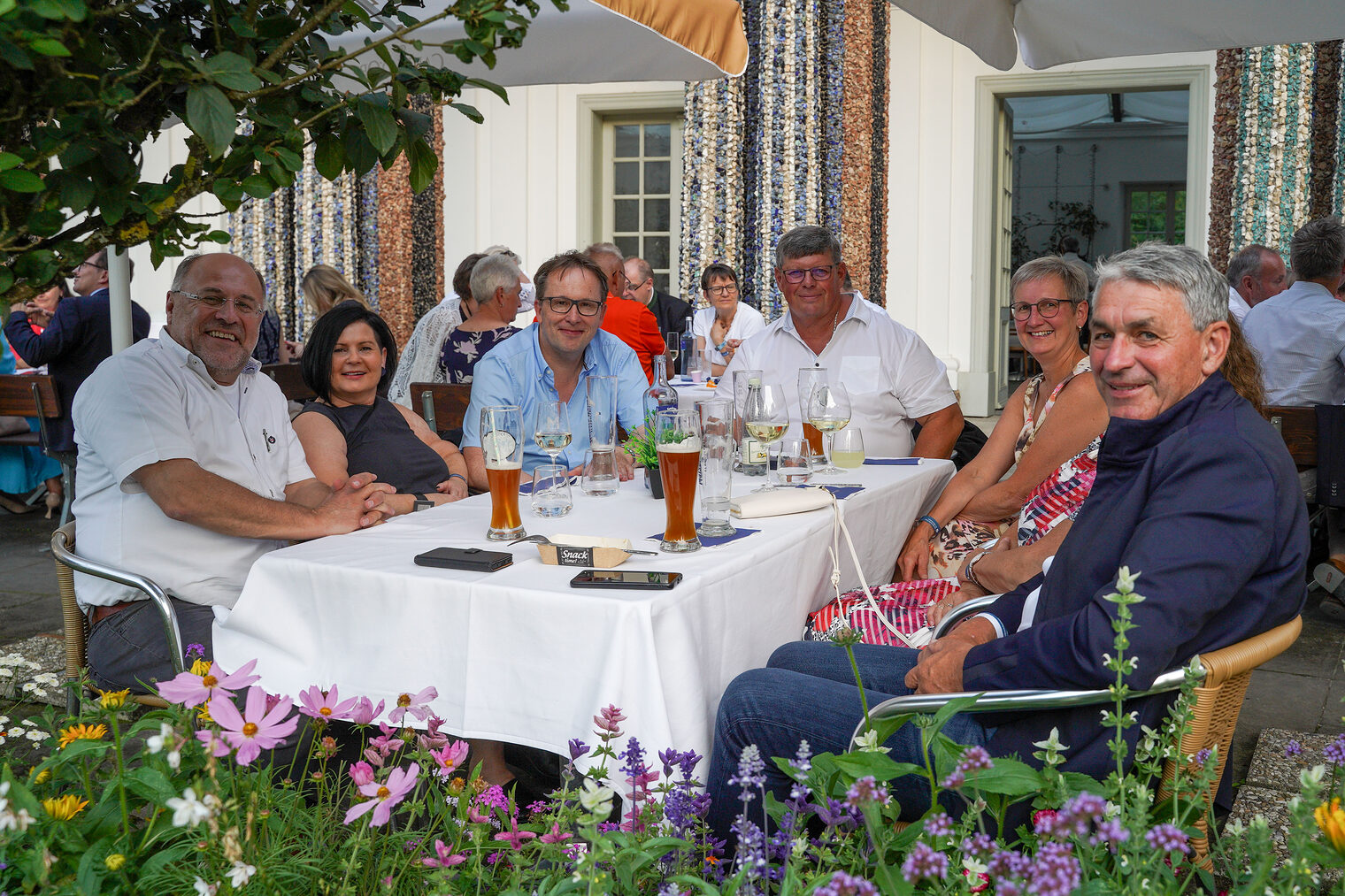Sechs Personen sitzen entspannt an einem gedeckten Tisch im Freien und genießen den Abend bei einem geselligen Treffen