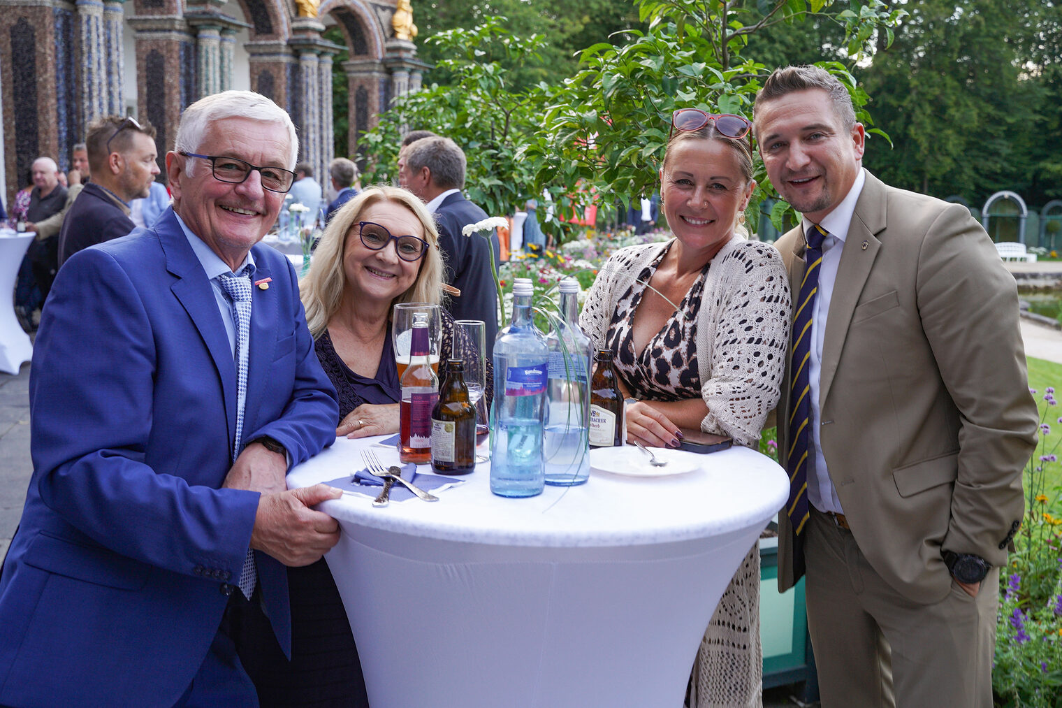 Zwei Herren und zwei Damen stehen um einen Stehtisch bei einer eleganten Veranstaltung im Freien und genießen die Atmosphäre