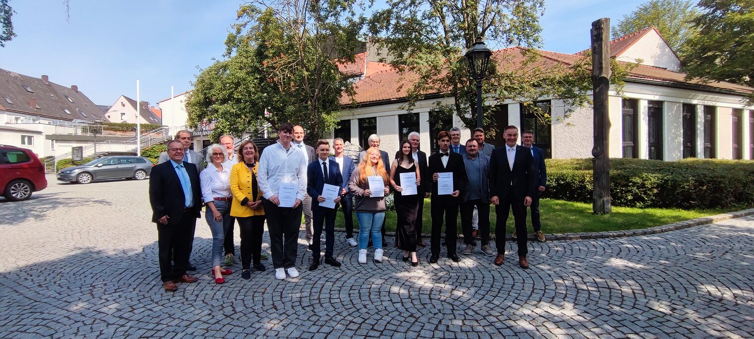 Gruppenfoto von Schülern mit Urkunden und Lehrern bei der Bestenehrung 2024 auf einem gepflasterten Platz vor einem Gebäude.