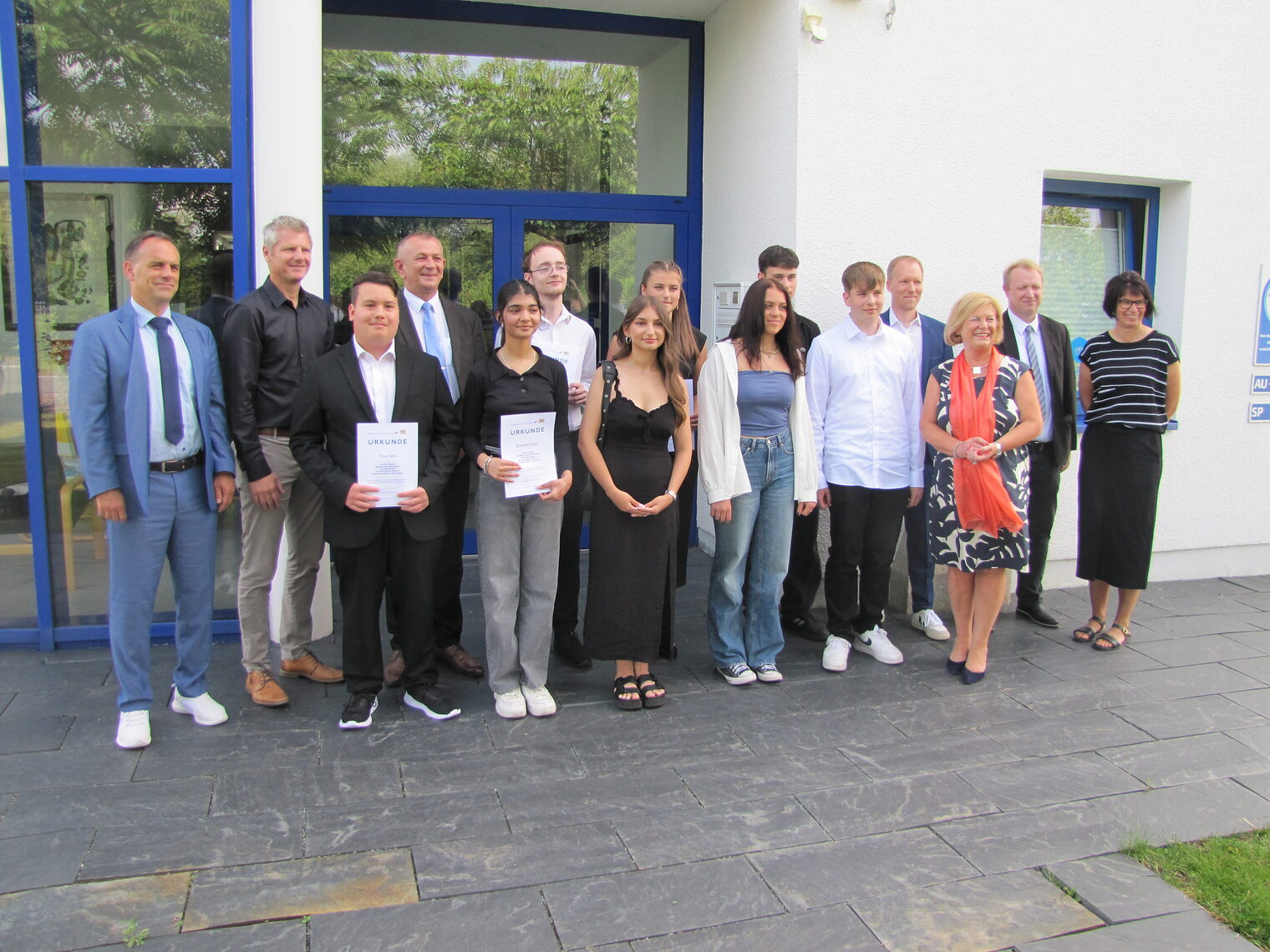 Gruppenfoto von Schülern mit Urkunden und Lehrern bei der Bestenehrung 2024 vor einem modernen Gebäude.