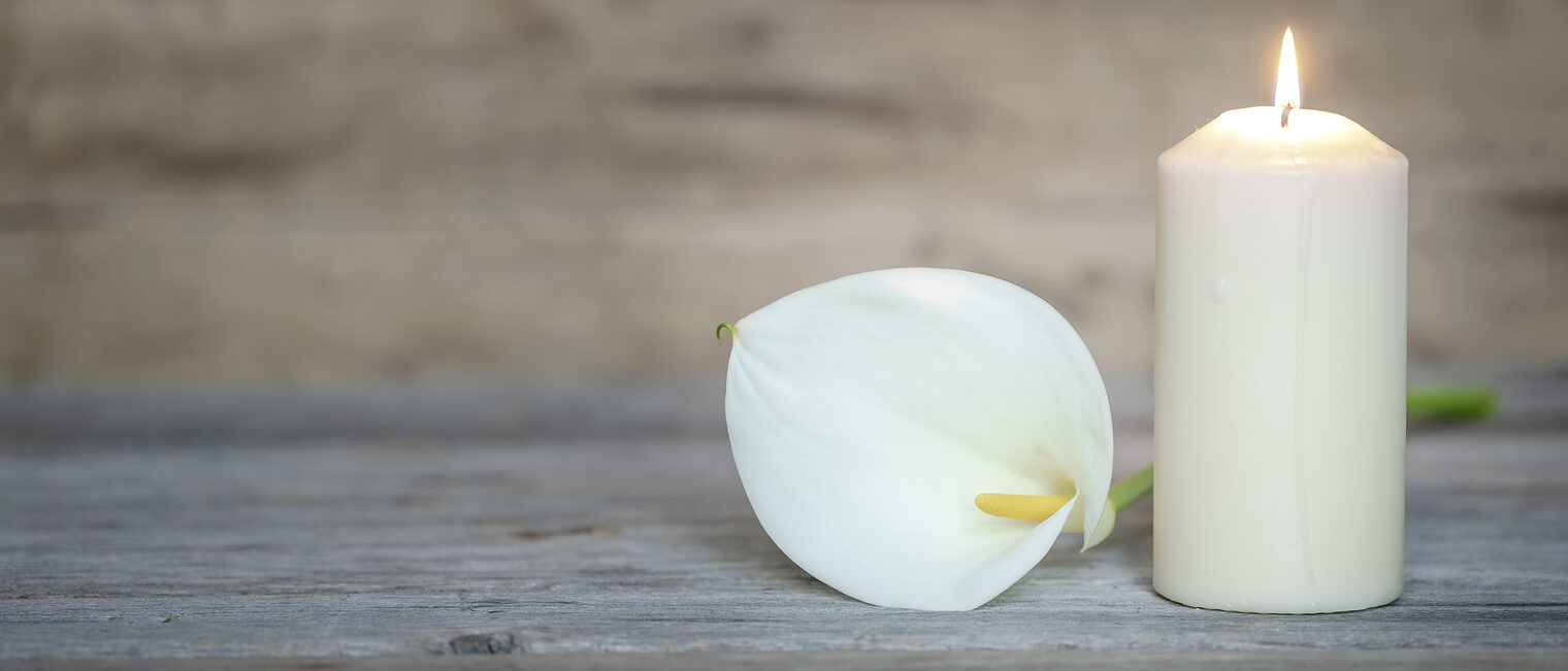 Weiße Kerze und weiße Calla-Lilie auf einem Holztisch, mit unscharfem Hintergrund.