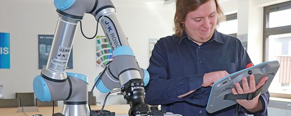 Mann bedient einen kollaborativen Roboterarm mit einem Touchscreen-Controller in einem modernen Laborumfeld.