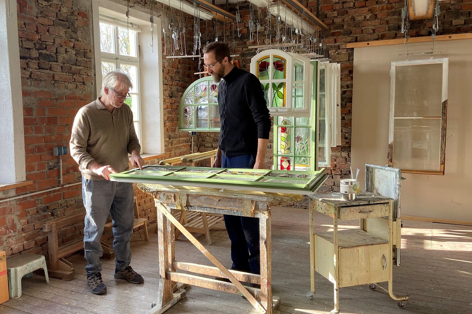 Das Bild zeigt den Restaurator Johannes Mosler mit Tischler Sebastian Freund. Sie begutachten gemeinsam ein historisches Fenster.