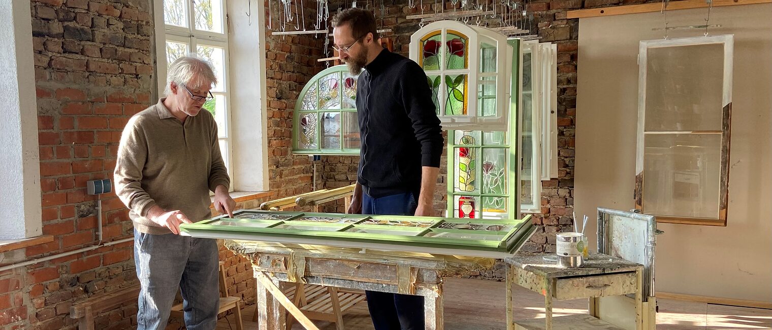 Eines der Community-Projekte von InTra-Bau beschäftigt sich damit, wie historische Fenster erhalten und energetisch verbessert werden können. Daran beteiligt ist beispielsweise Restaurator Johannes Mosler – hier im Bild mit Tischler Sebastian Freund Das Bild zeigt den Restaurator Johannes Mosler mit Tischler Sebastian Freund. Sie begutachten gemeinsam ein historisches Fenster.
