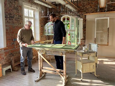 Eines der Community-Projekte von InTra-Bau beschäftigt sich damit, wie historische Fenster erhalten und energetisch verbessert werden können. Daran beteiligt ist beispielsweise Restaurator Johannes Mosler – hier im Bild mit Tischler Sebastian Freund Das Bild zeigt den Restaurator Johannes Mosler mit Tischler Sebastian Freund. Sie begutachten gemeinsam ein historisches Fenster.