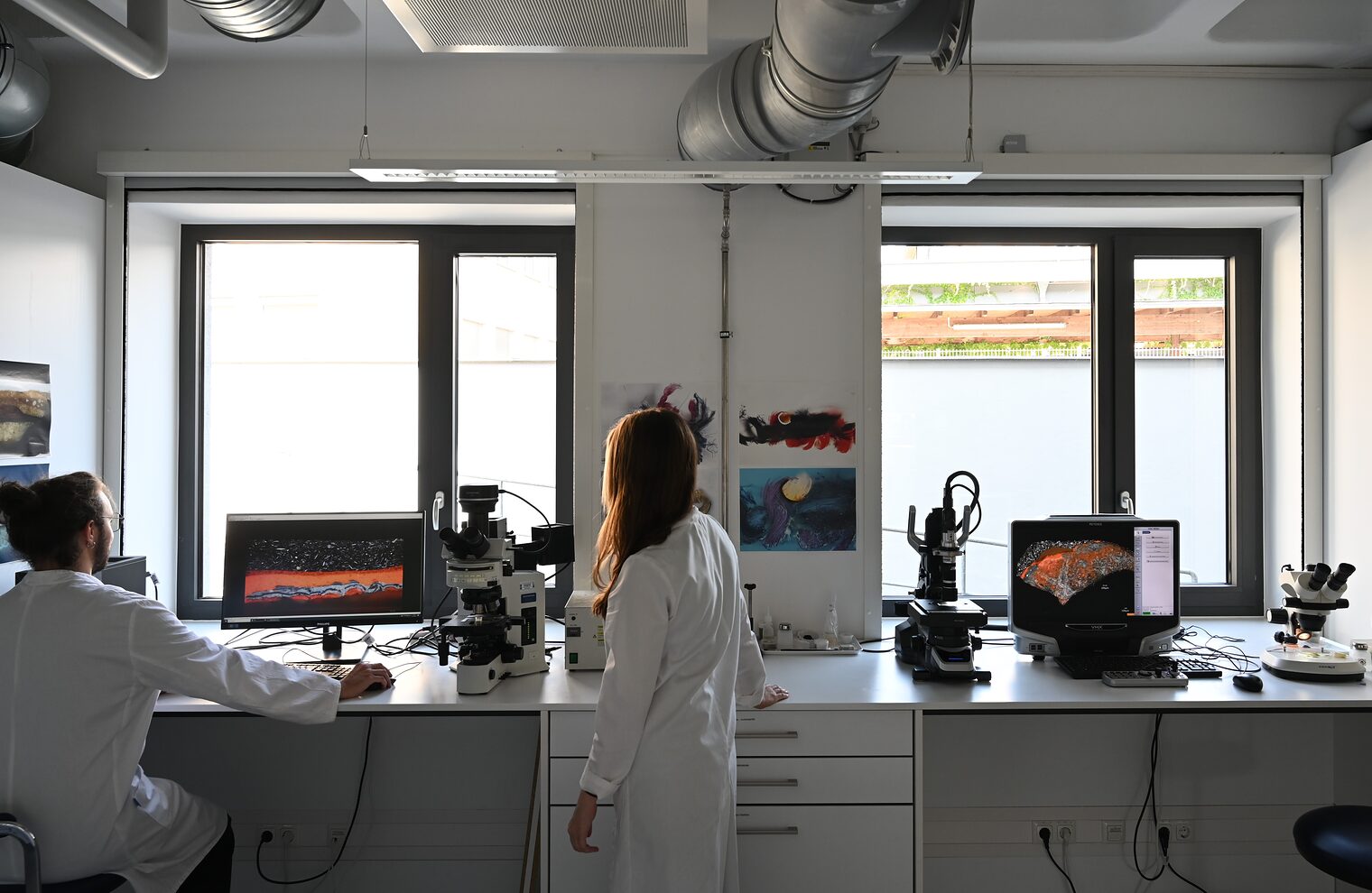 Das Bild zeigt ein Labor, in dem zwei Mitarbeitende an Apparaturen chemische Analysen machen.