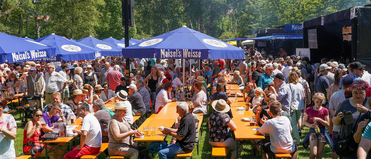 Besucher des Bratwurstgipfels sitzen auf Bierbänken und essen und trinken an Tischen.