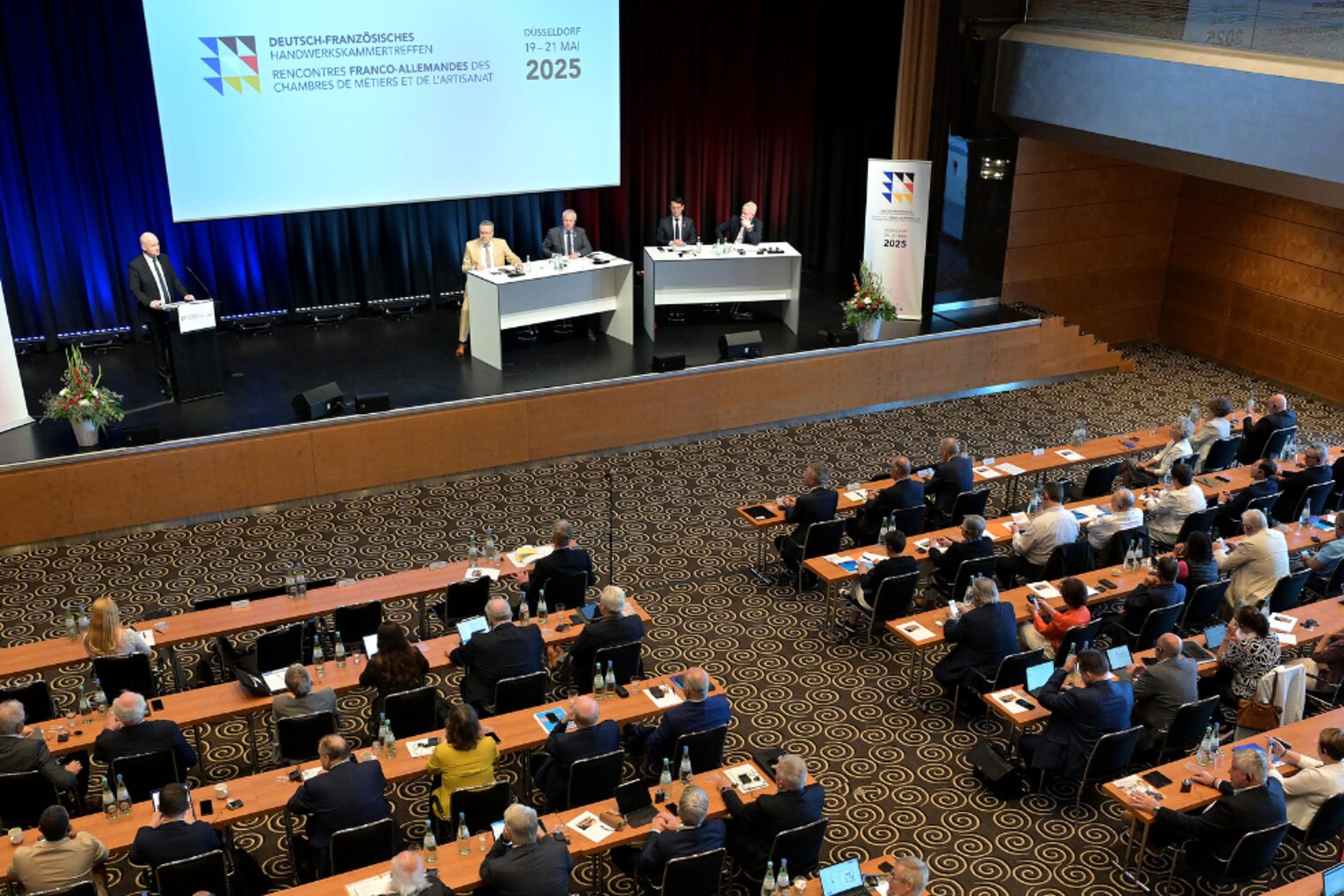 Die Vertreter der Handwerkskammern sitzen in einem Tagungsraum vor einem Podium mit einer Präsentation.