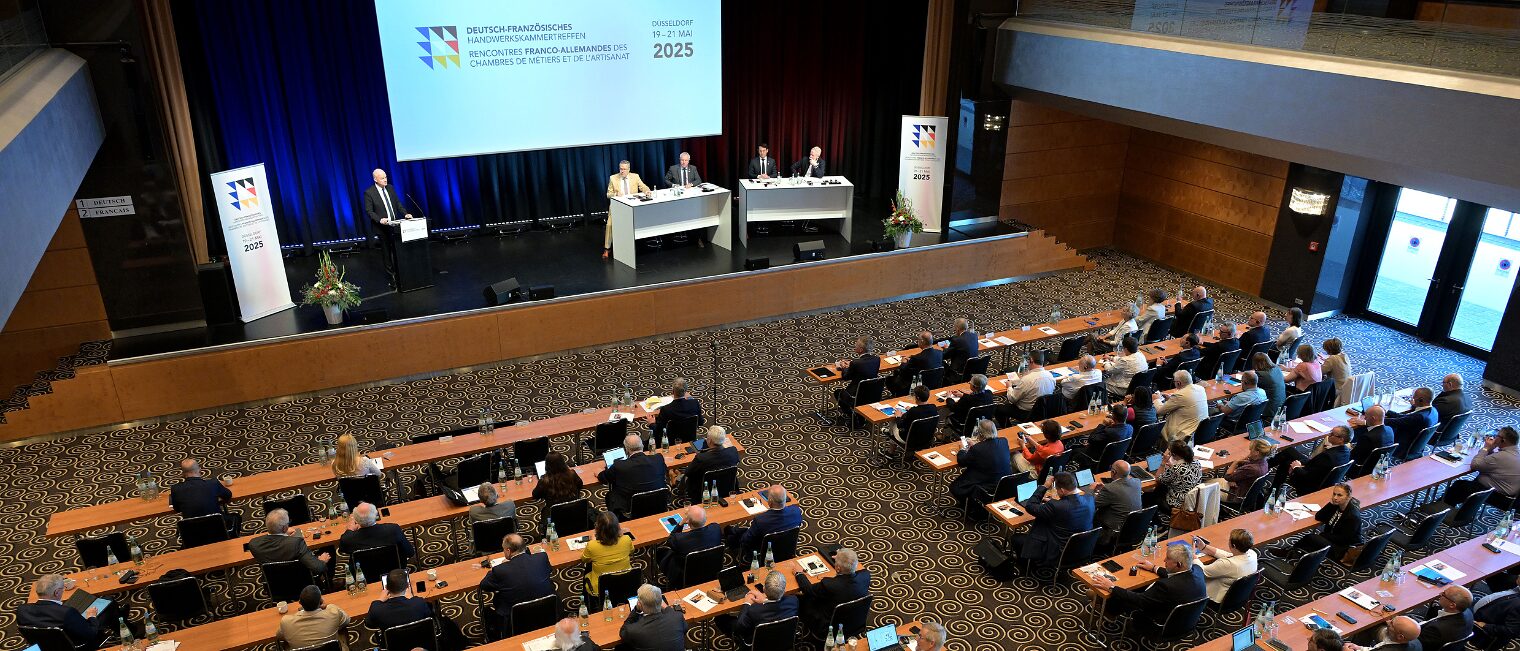 Die Vertreter der Handwerkskammern sitzen in einem Tagungsraum vor einem Podium mit einer Präsentation.