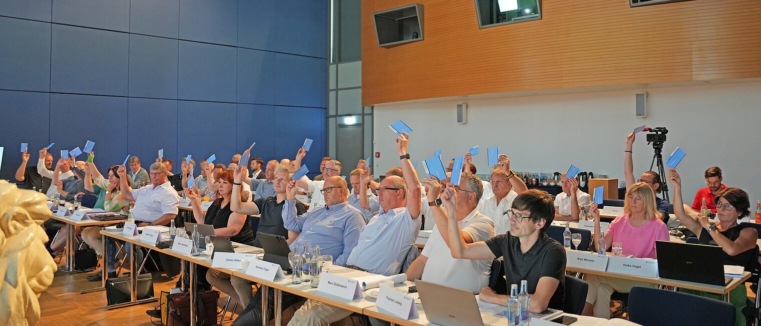 Mitglieder der Vollversammlung der Handwerkskammer für Oberfranken stimmen in einem Sitzungssaal per Handzeichen ab.