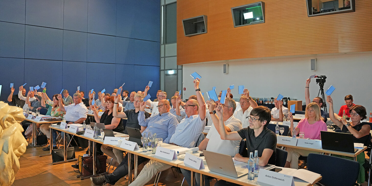 Mitglieder der Vollversammlung der Handwerkskammer für Oberfranken stimmen in einem Sitzungssaal per Handzeichen ab.