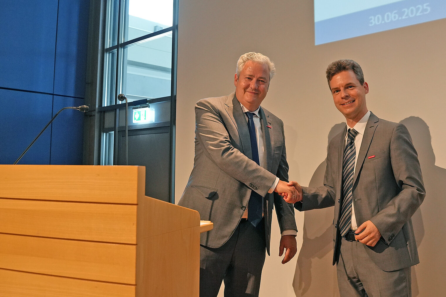 Matthias Graßmann schüttelt Sebastian Serfas neben einem Podium die Hand.