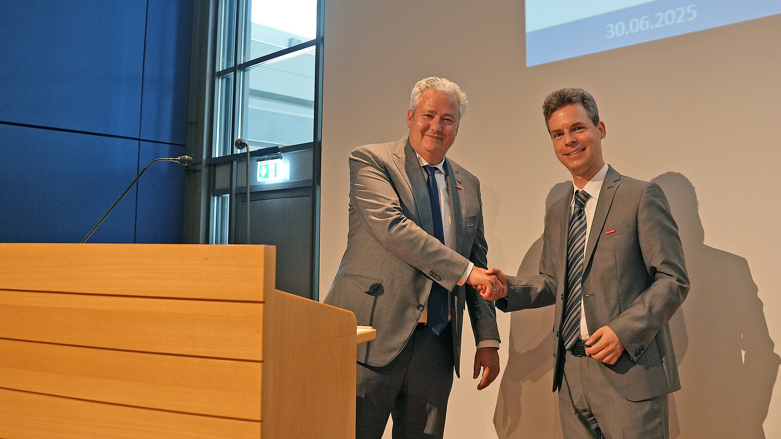 Matthias Graßmann schüttelt Sebastian Serfas neben einem Podium die Hand.