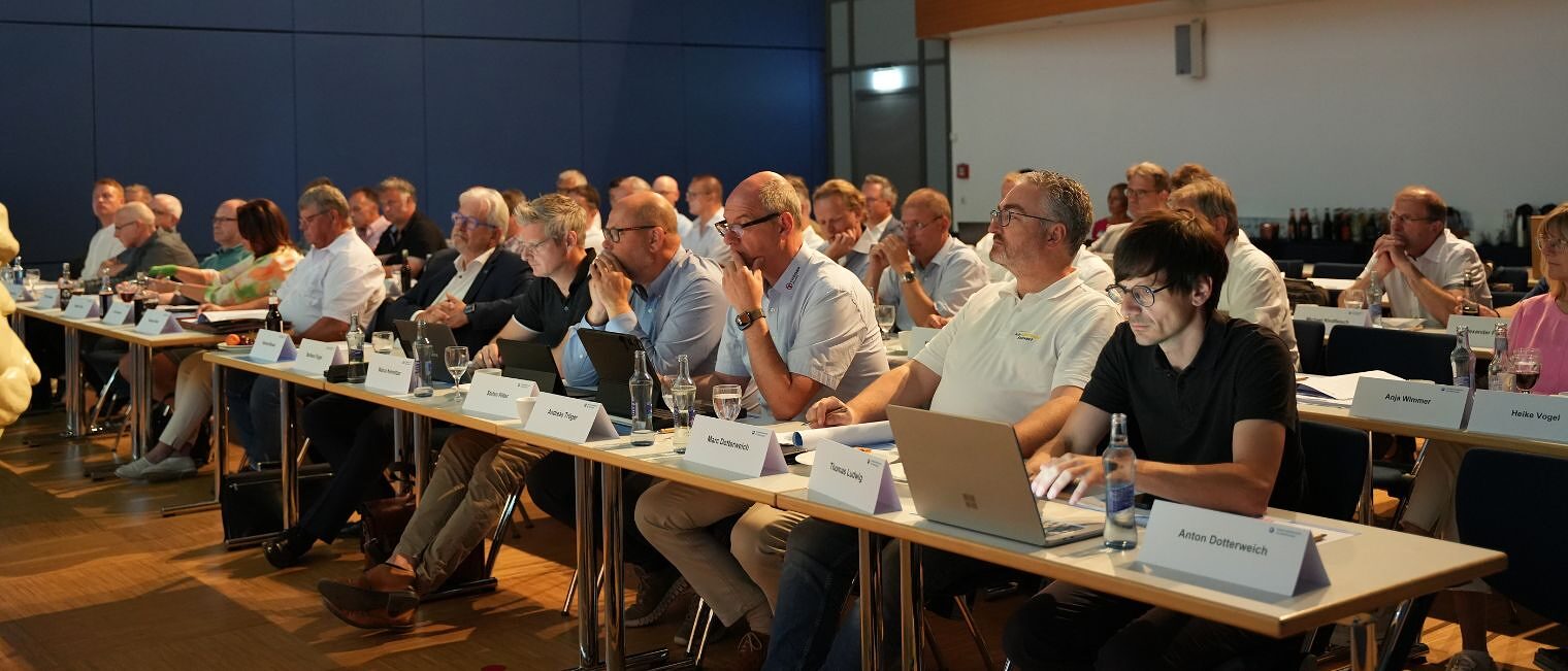 Die Mitglieder der Vollversammlung sitzen an Tischen in einem Sitzungssaal.