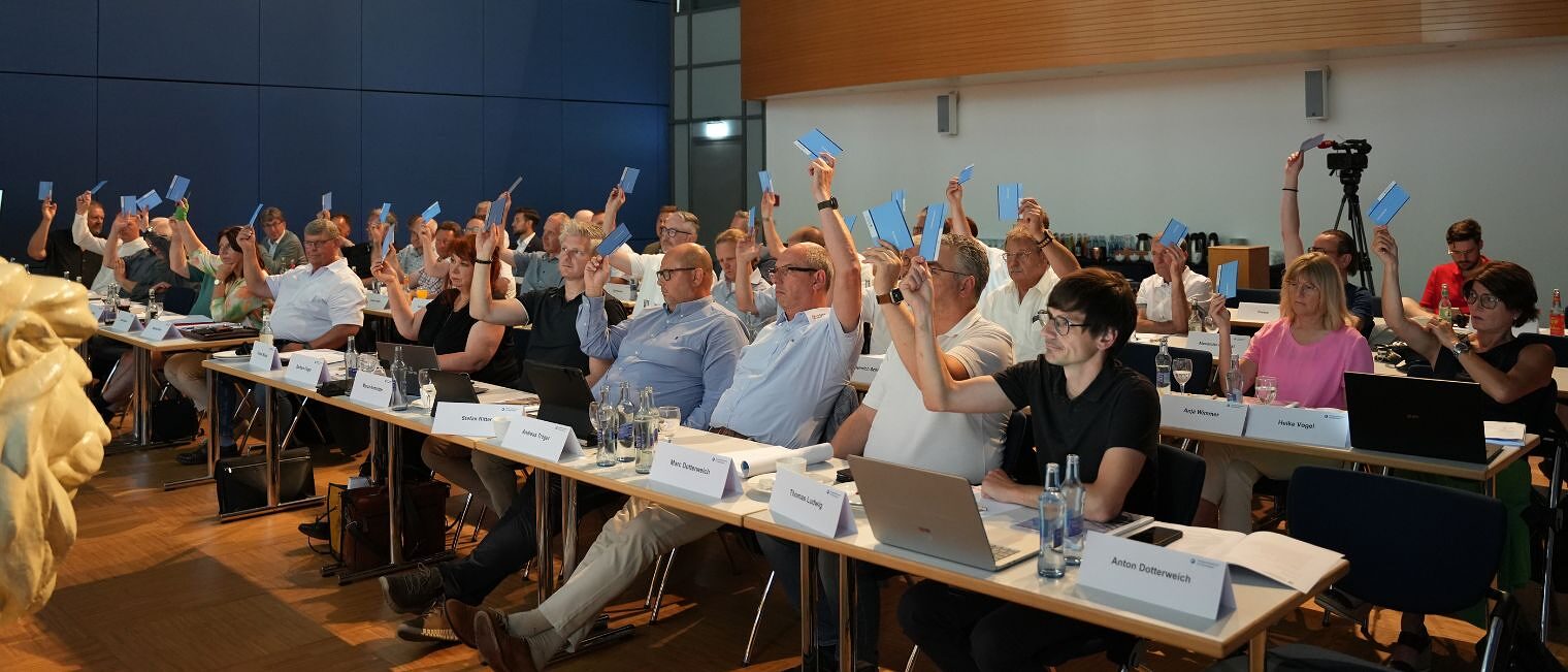 Die Mitglieder der Vollversammlung stimmen per Handzeichen in einem Sitzungssaal ab.