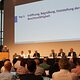 Der Vorstand und die Geschäftsführung der Handwerkskammer für Oberfranken sitzt an einem Tisch auf einem Podium vor der Vollversammlung.