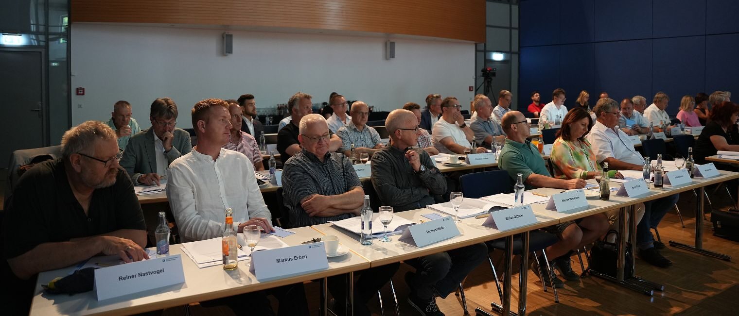 Mitglieder der Vollversammlung der Handwerkskammer für Oberfranken sitzen an Tischen und hören dem Vortragenden zu.