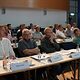 Mitglieder der Vollversammlung der Handwerkskammer für Oberfranken sitzen an Tischen und hören dem Vortragenden zu.