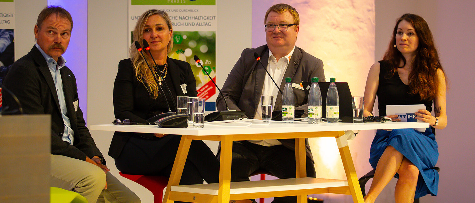 Sergio Drawert, Nicole Wagner, Johannes Lange und Sandra Peter hören auf dem Podium dem Vortrag zu.