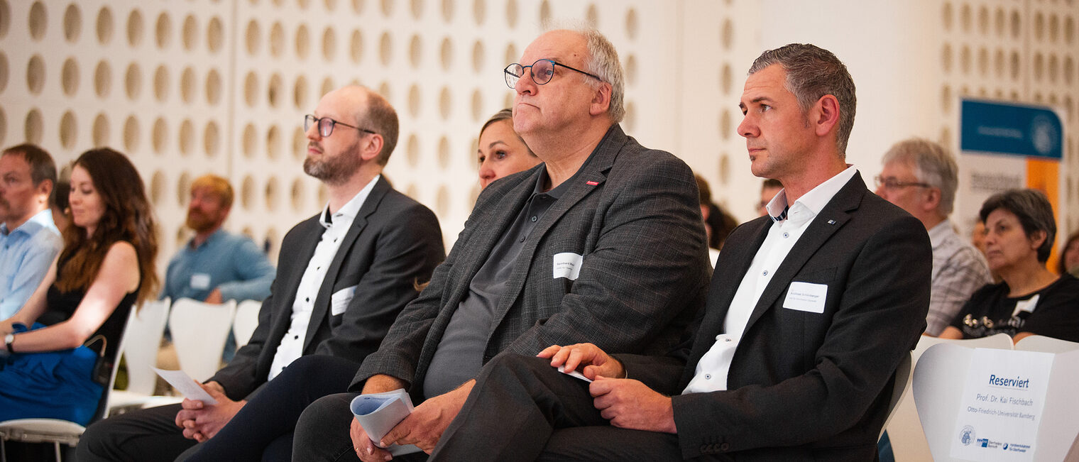 Professor Schiemann, Reinhard Bauer und Andreas Schönberger hören im Publikum zu. 