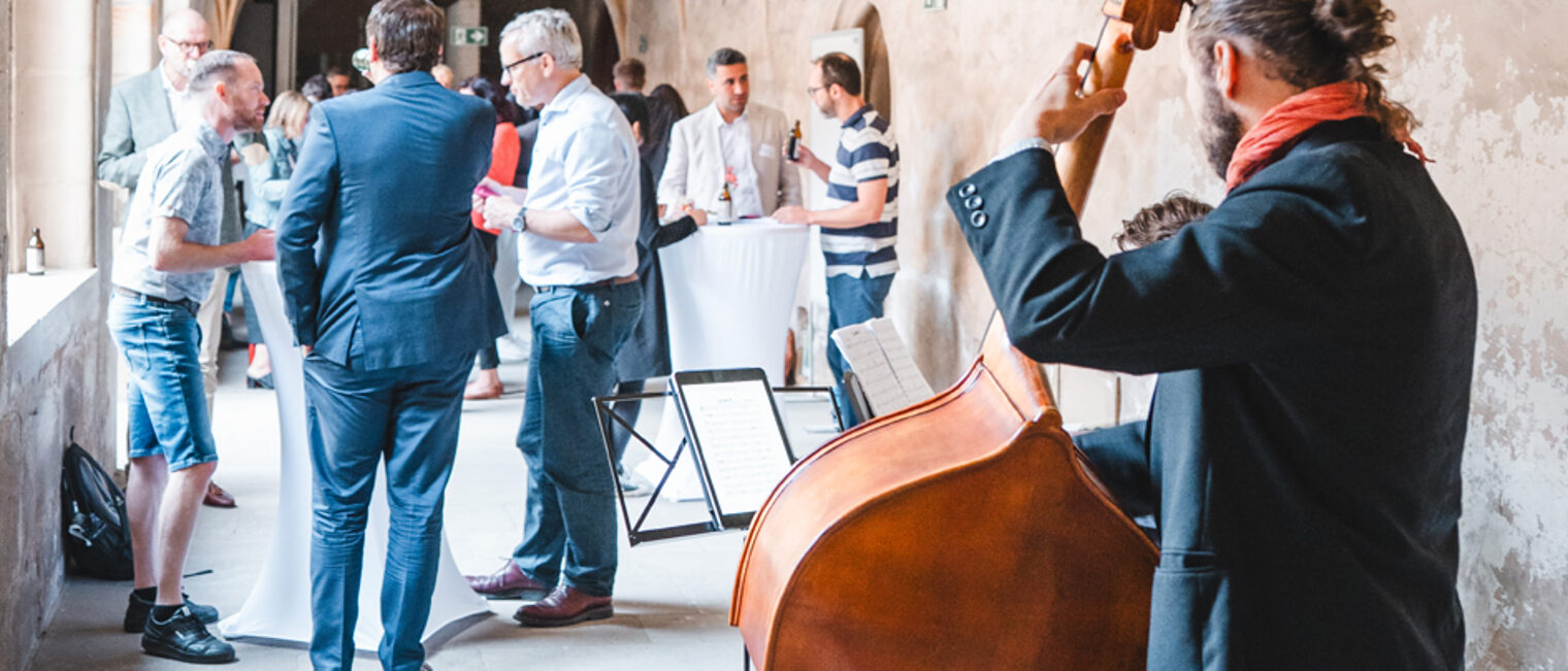 Die Gäste der Tandem-Reihe unterhalten sich, während ein Mann Cello spielt.