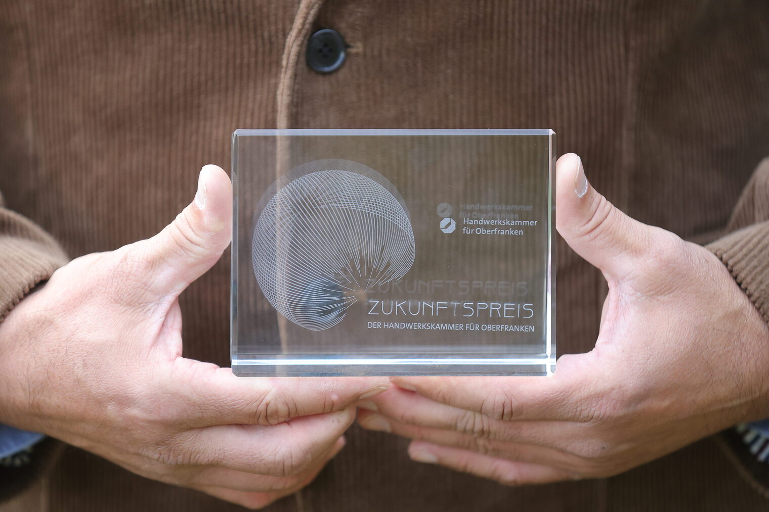 Eine Person hält die Trophäe des Zukunftspreises 2025 in den Händen. 