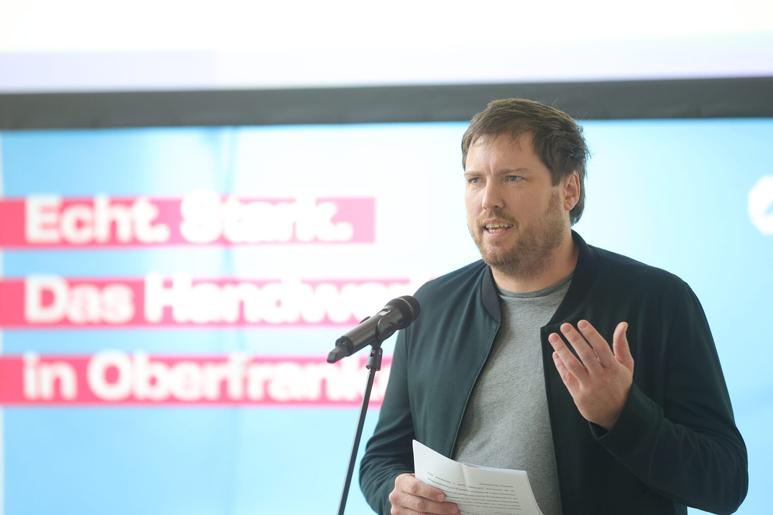Manuel Wolz spricht in ein Mikrofon auf der Bühne.