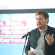 Manuel Wolz spricht in ein Mikrofon auf der Bühne.