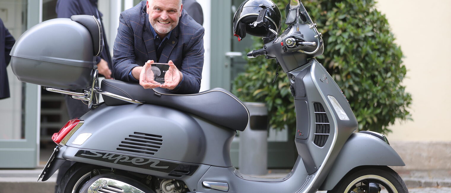 Wolfgang Fösel posiert mit seinem Zukunftspreis und einer Vespa.