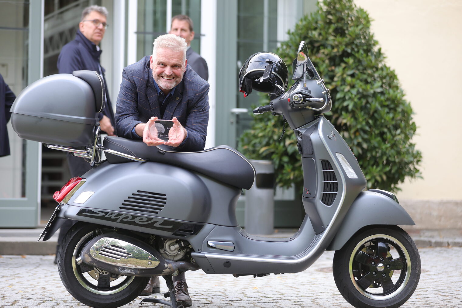 Wolfgang Fösel posiert mit seinem Zukunftspreis und einer Vespa.