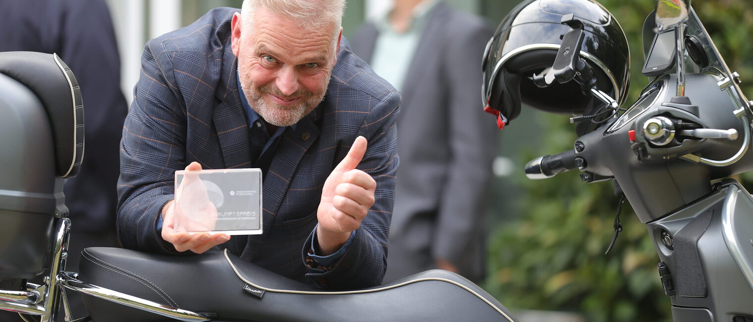 Wolfgang Fösel präsentiert an seiner Vespa seinen Zukunftspreis.