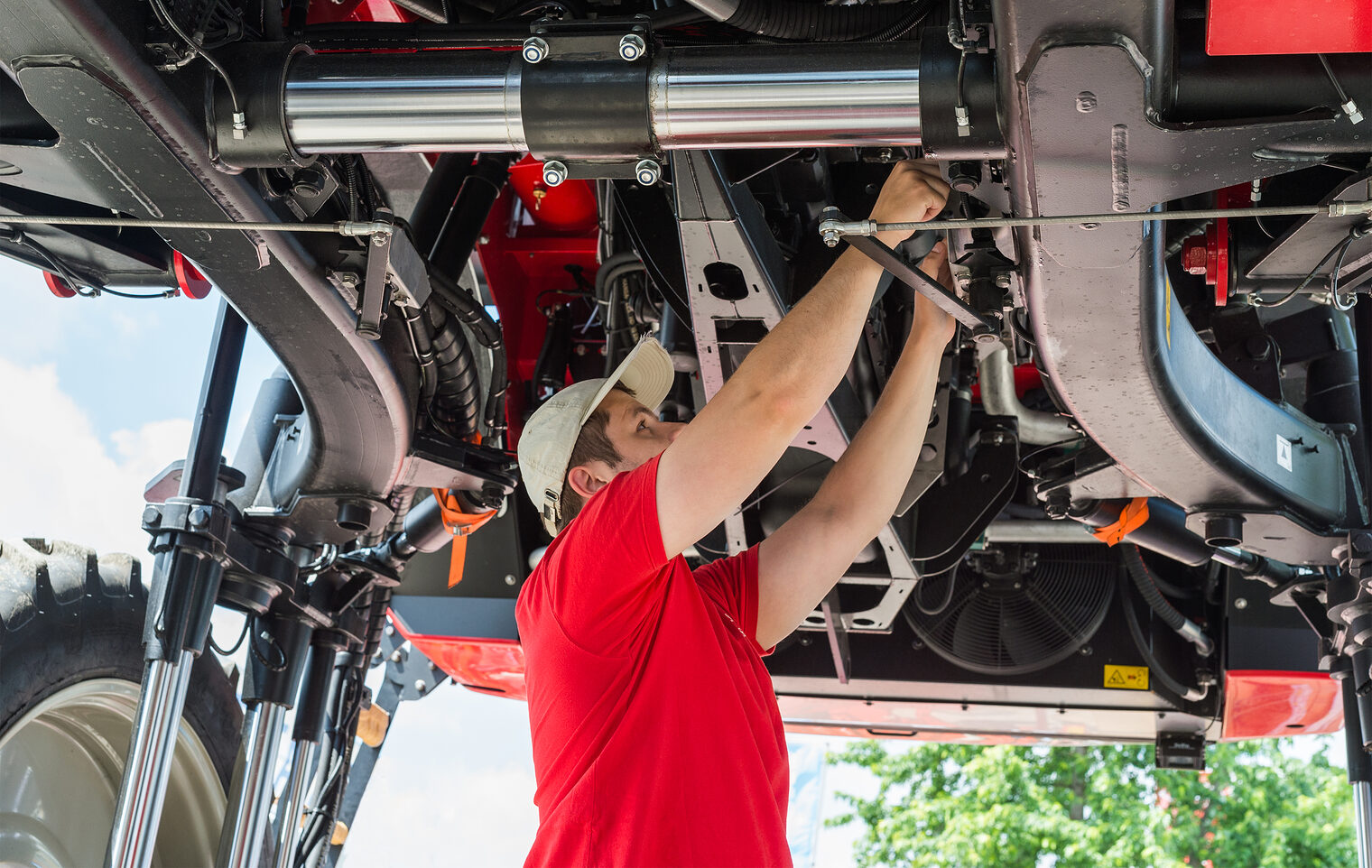 Ein Landmaschinenmechaniker schraubt am Unterboden eines Traktors etwas fest.