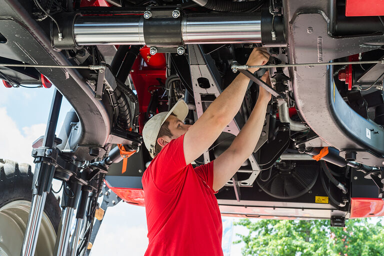 Ein Landmaschinenmechaniker schraubt am Unterboden eines Traktors etwas fest.