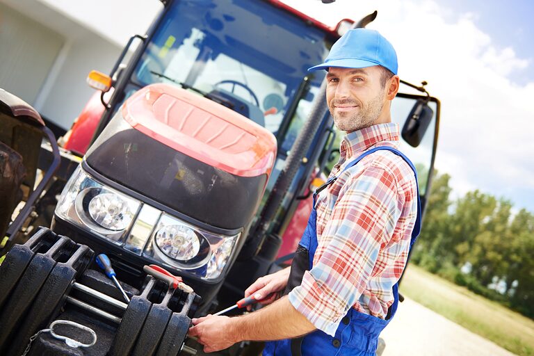 Ein Landmaschinenmechatroniker schraubt mit einem Schraubenschlüssel etwas an einem Traktor fest.