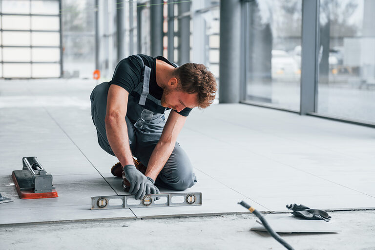 Ein junger Fliesenleger prüft mit einer Wasserwaage ob die Fließen gerade sind.