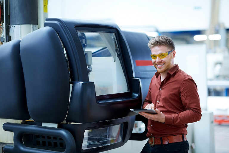 Ein junger Metallbauermeister benutzt ein Tablet um eine Maschine zu steuern.