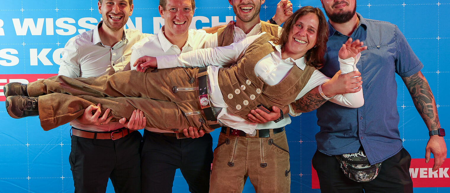 Eine Gruppe von Meisterschülern und Freunden posiert vor einer Fotowand.