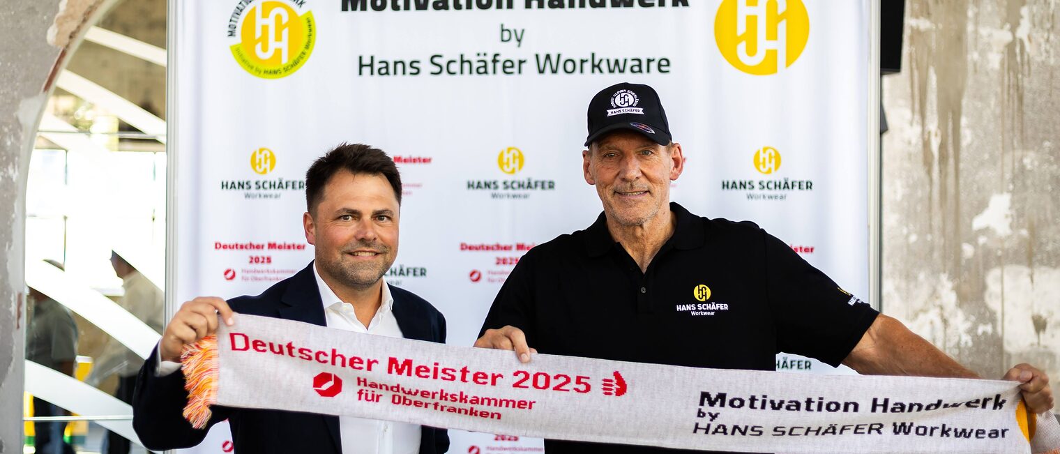 Andreas Grewe und Ralf Moeller posieren vor einer Fotowand mit einem Meisterschal.
