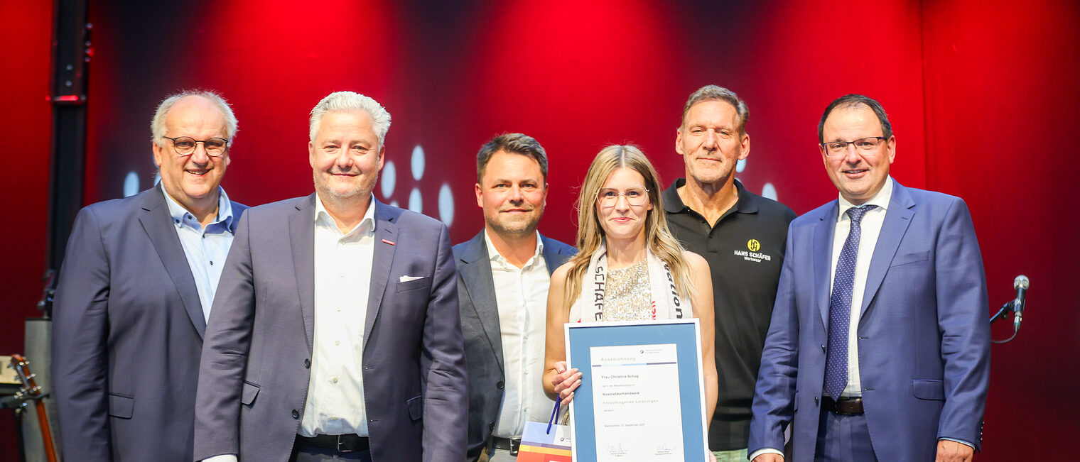 Kosmetikermeisterin Christina Schug präsentiert ihre Urkunde mit Reinhard Bauer, Matthias Graßmann, Andreas Grewe, Martin Schöffel und Ralf Moeller.