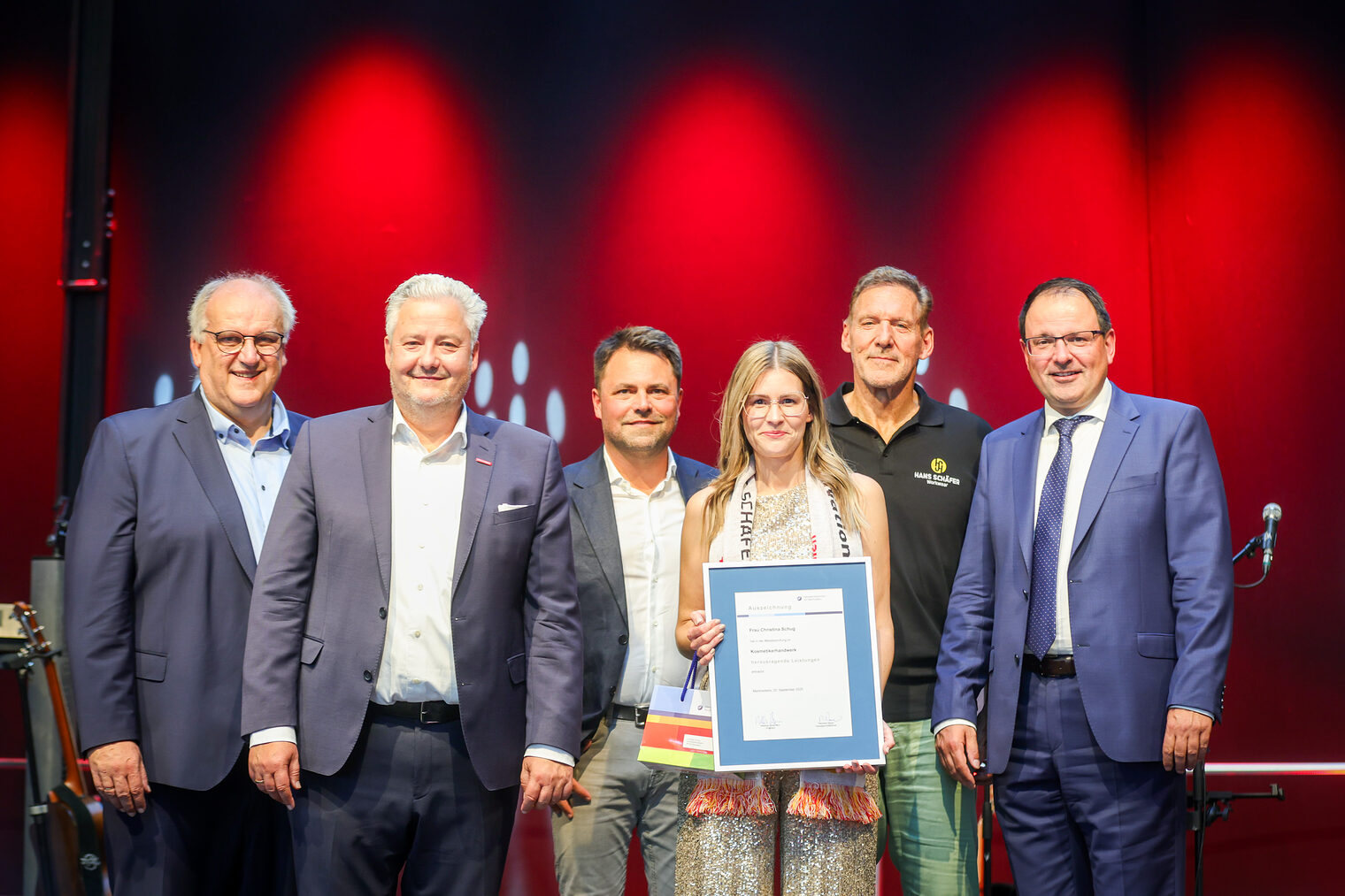 Kosmetikermeisterin Christina Schug präsentiert ihre Urkunde mit Reinhard Bauer, Matthias Graßmann, Andreas Grewe, Martin Schöffel und Ralf Moeller.