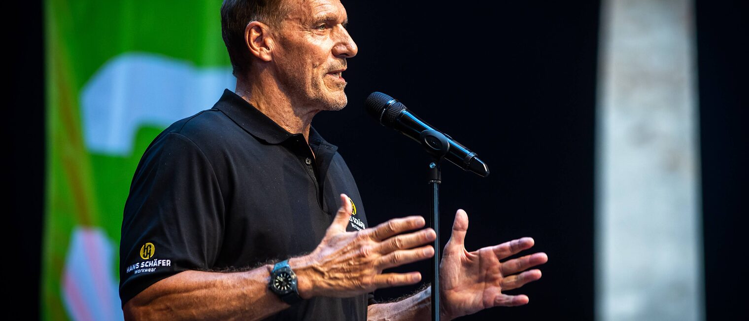 Ralf Moeller spricht auf der Bühne in ein Mikrofon.
