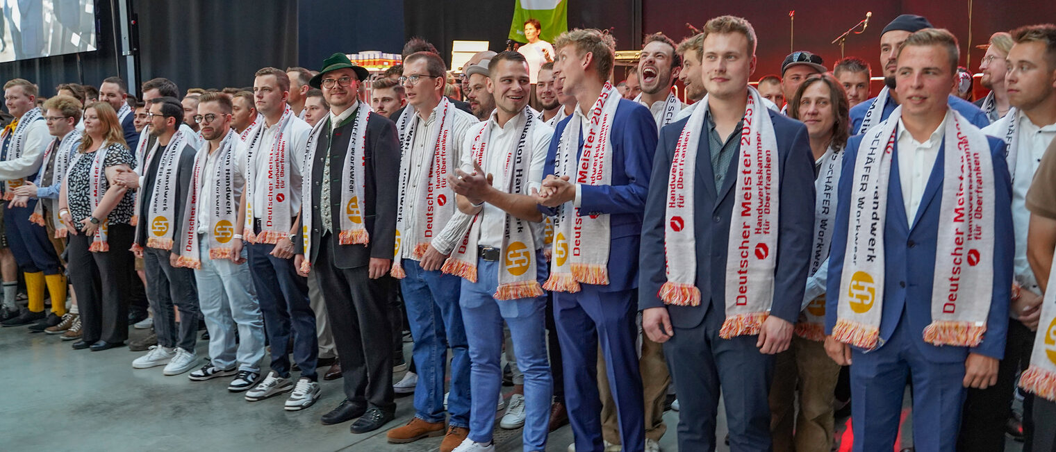 Die Meisterinnen und Meister stehen mit ihren Schals vor der Bühne.