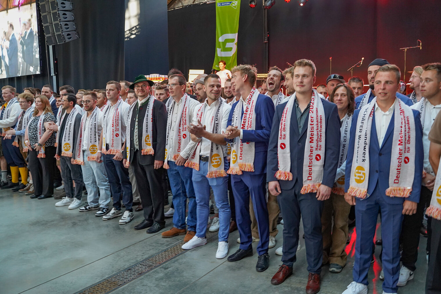 Die Meisterinnen und Meister stehen mit ihren Schals vor der Bühne.