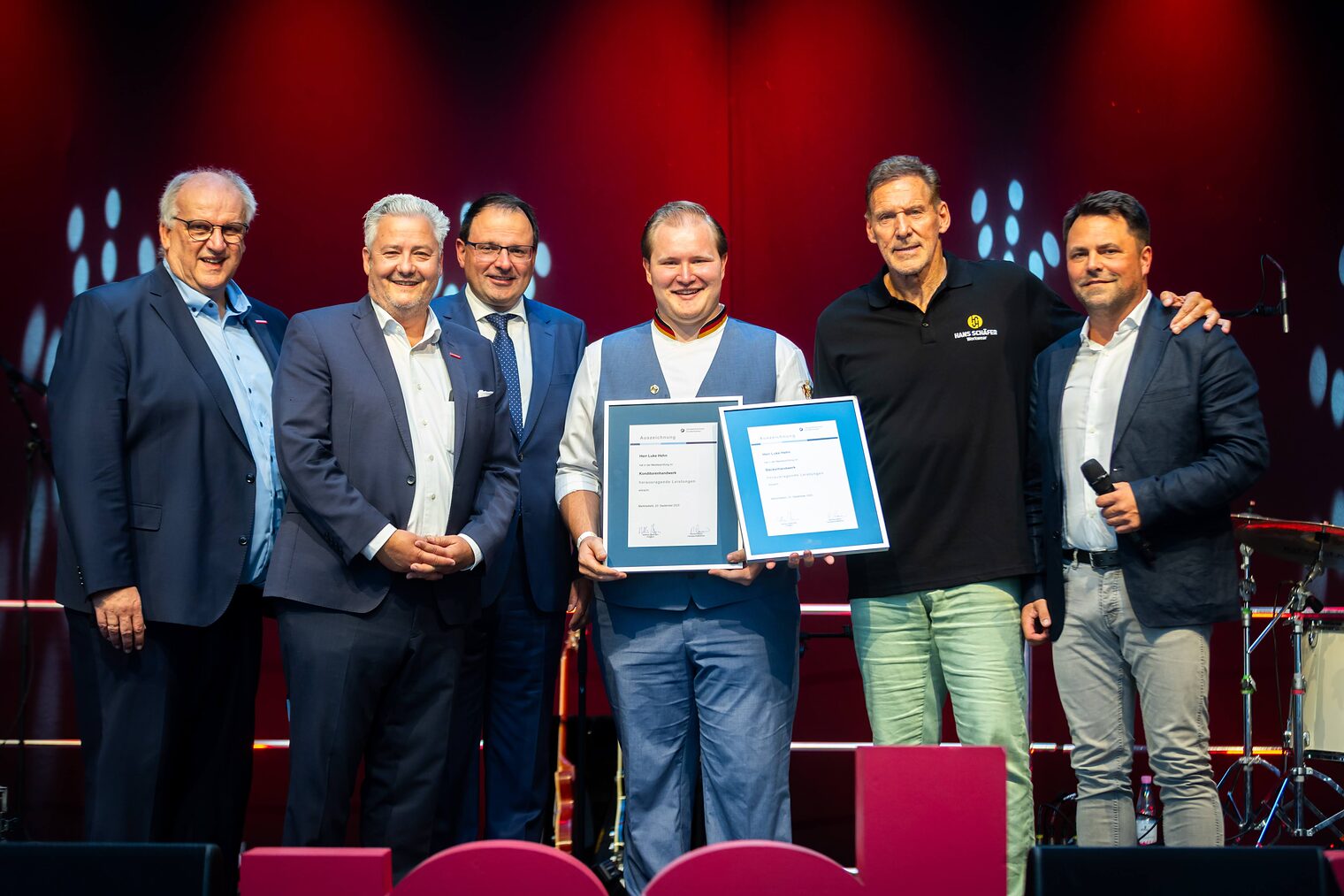 Bäcker- und Konditormeister Luke Hehn präsentiert seine zwei Bestenurkunden mit Reinhard Bauer, Matthias Graßmann, Martin Schöffel, Ralf Moeller und Andreas Grewe