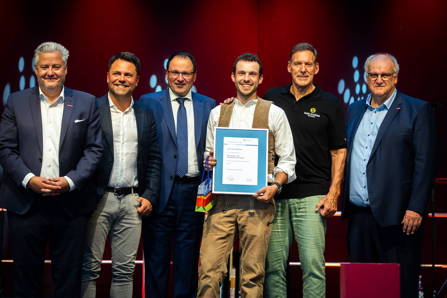Steinmetzmeister Lukas Mutschler präsentiert seine Bestenurkunde mit Matthias Graßmann, Andreas Grewe, Martin Schöffel, Ralf Moeller und Reinhard Bauer
