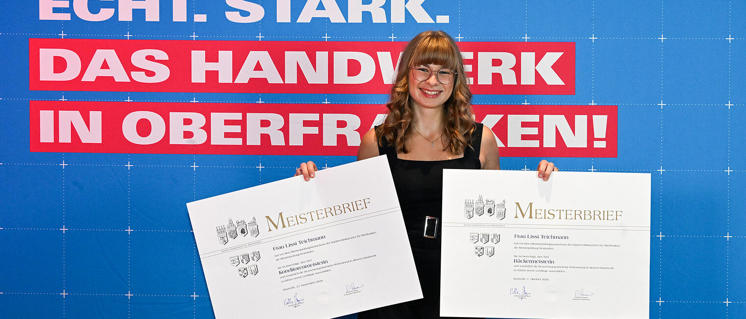 Lissi Teichmann posiert mit ihren Meisterbriefen vor einer Fotowand.