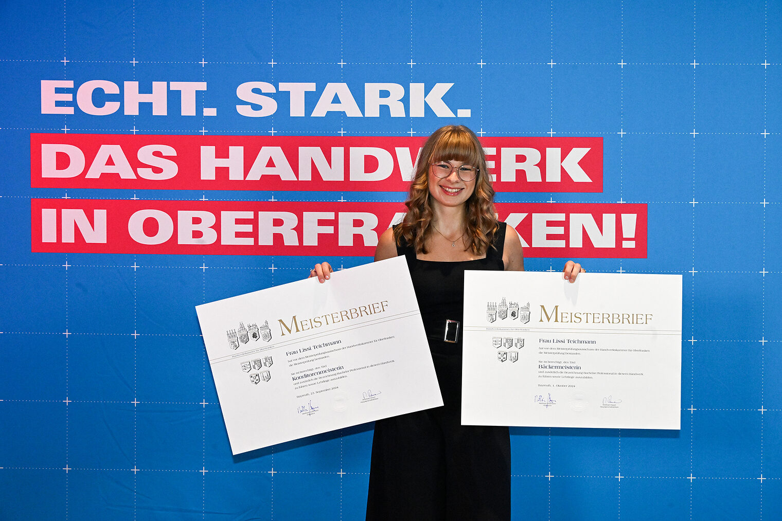 Lissi Teichmann posiert mit ihren Meisterbriefen vor einer Fotowand. 
